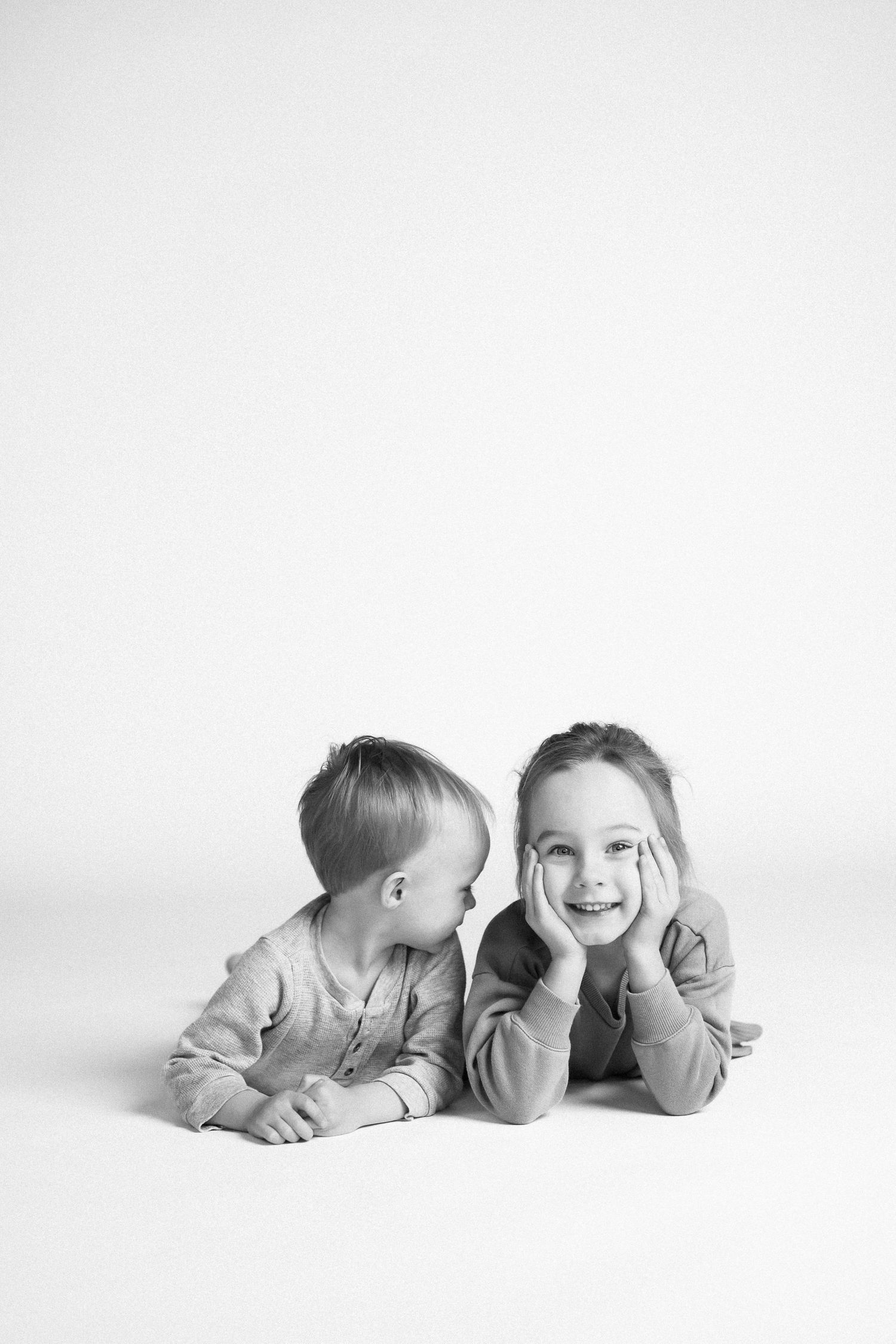 Two children laying side by side on white background with playful expressions.