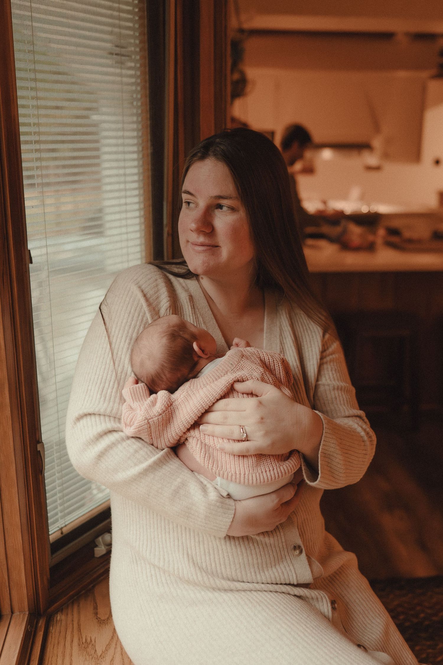 Parent in cream sweater sharing loving moments with newborn in soft window light.