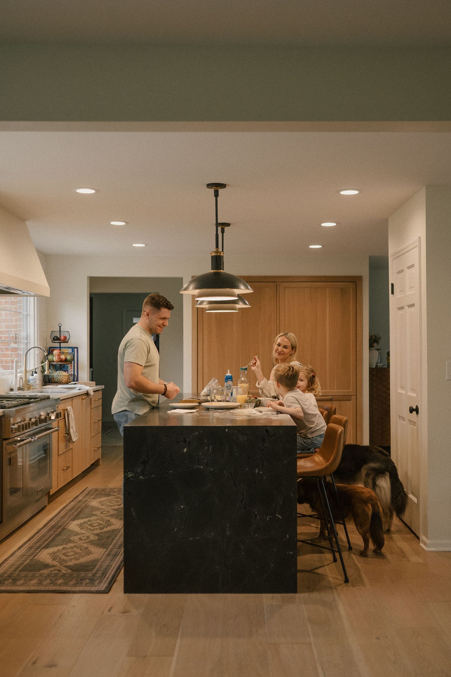 Family gathered around a dark marble kitchen island with pendant lighting in a modern home.