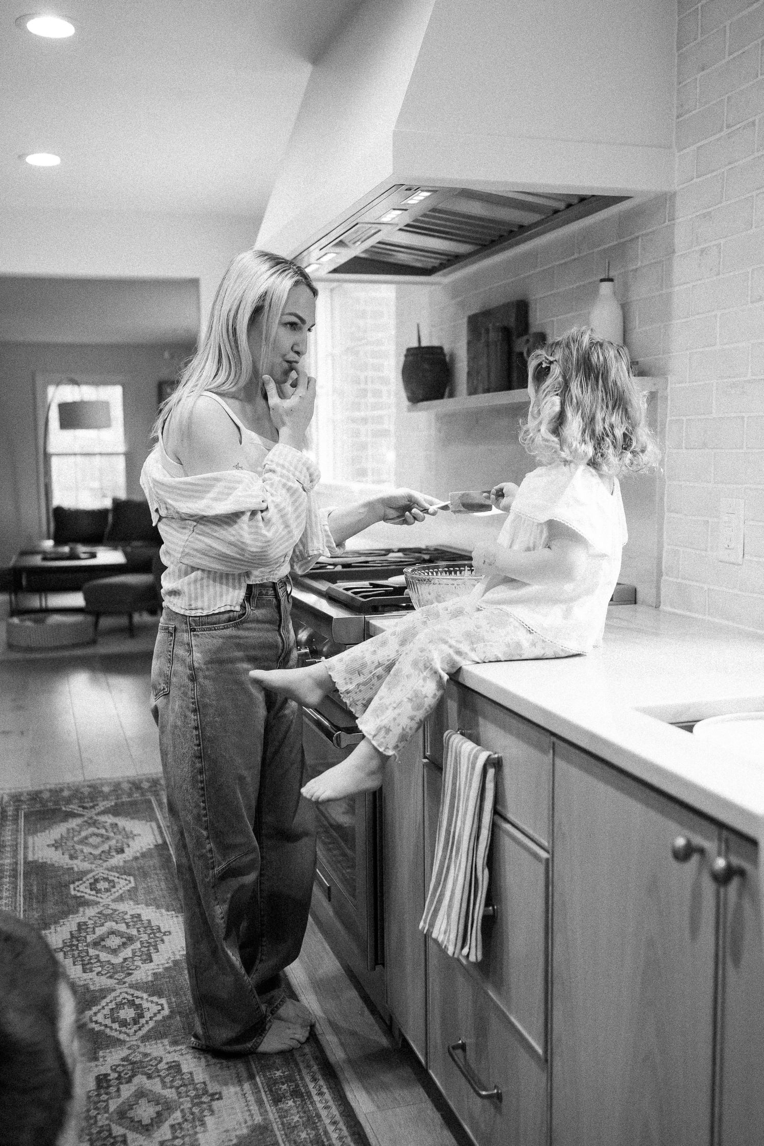 Black and white photo of a mother and daughter sharing a joyful moment by the kitchen stove.