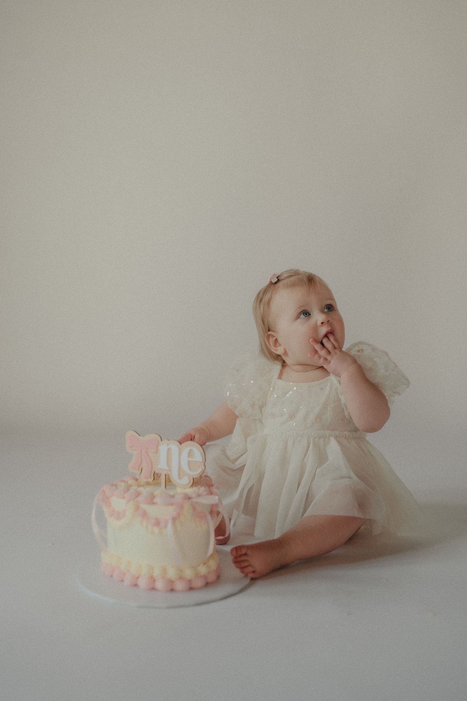 Adorable baby girl in white tulle dress smashes pink and yellow first birthday cake during cake smash photo.