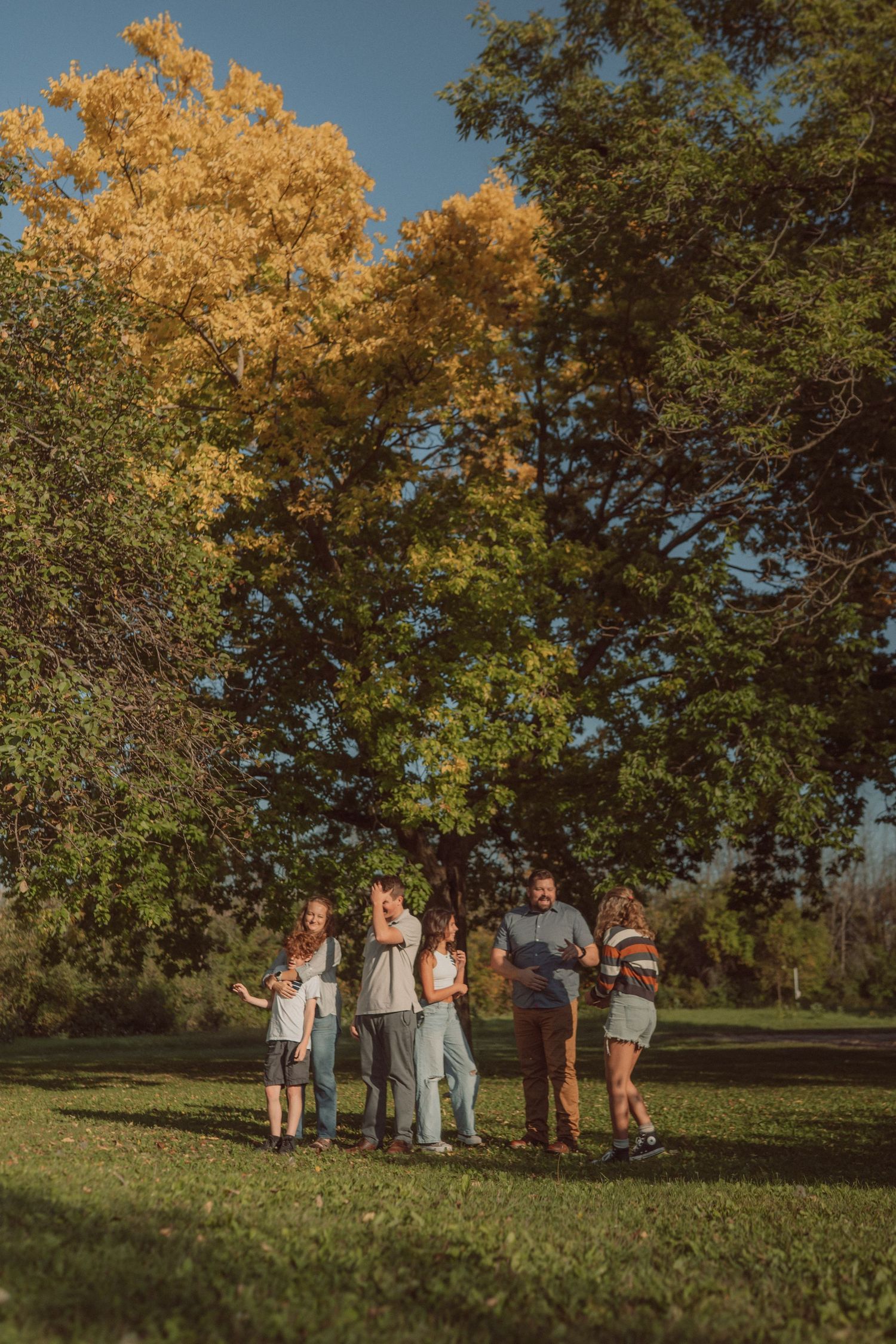 Group gathering under golden autumn trees in park setting during sunset.