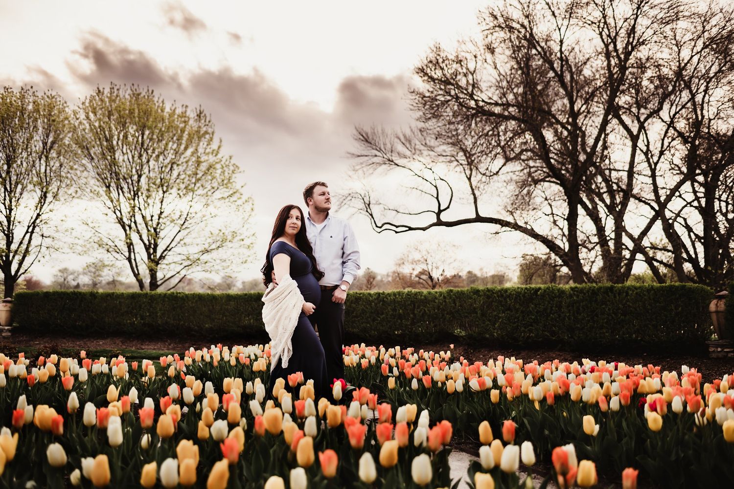 Couple standing together in field of vibrant orange and white tulips at dusk.