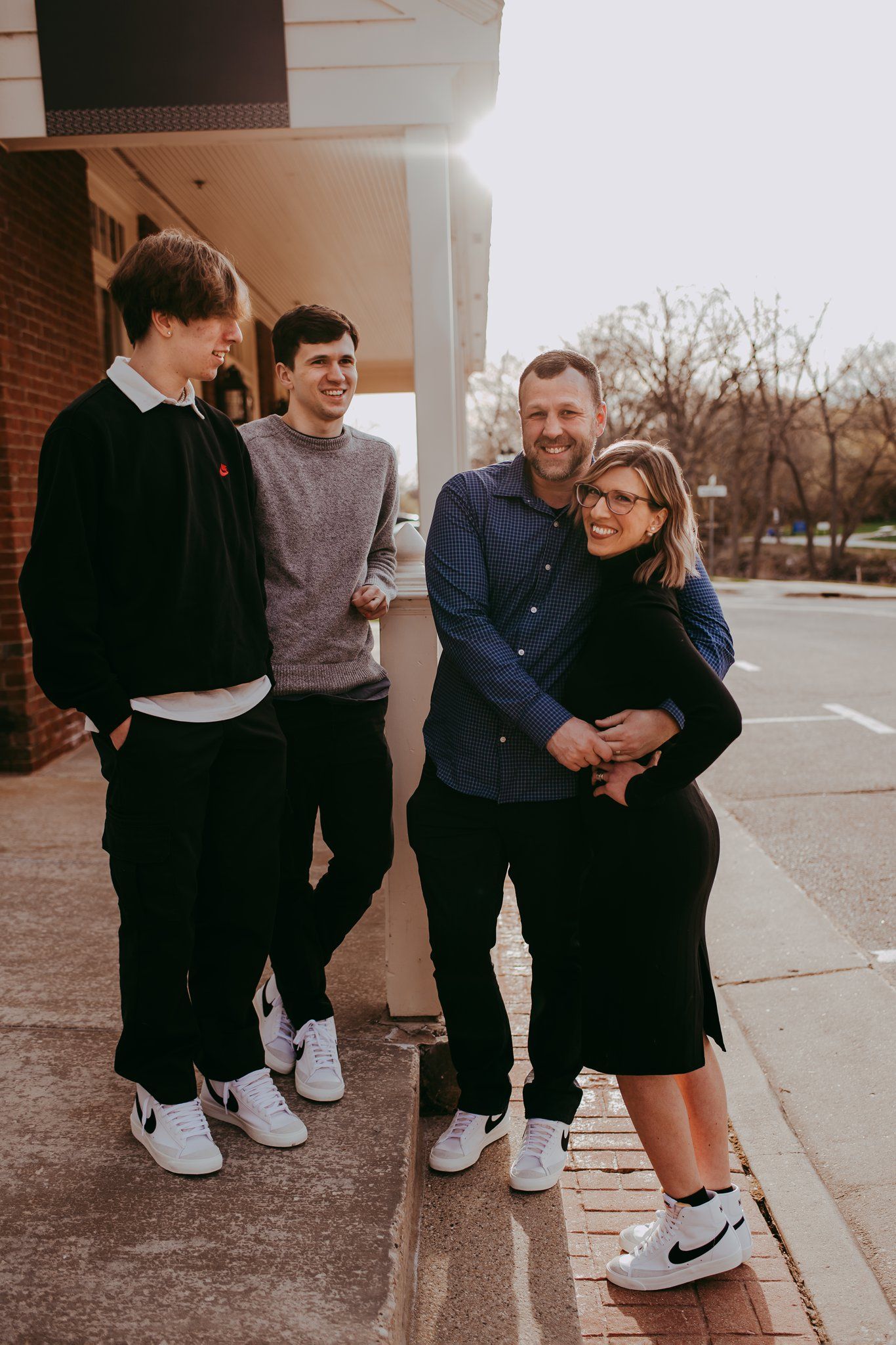 A group in casual attire poses together on a brick sidewalk under an overhanging roof.