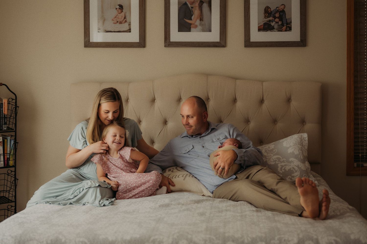 Lifestyle family portrait on bed with framed photos on wall behind.