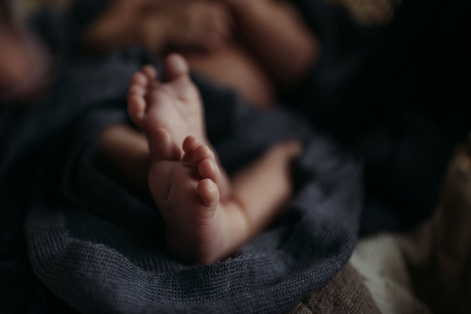 Small baby feet peek out from dark textured fabric.