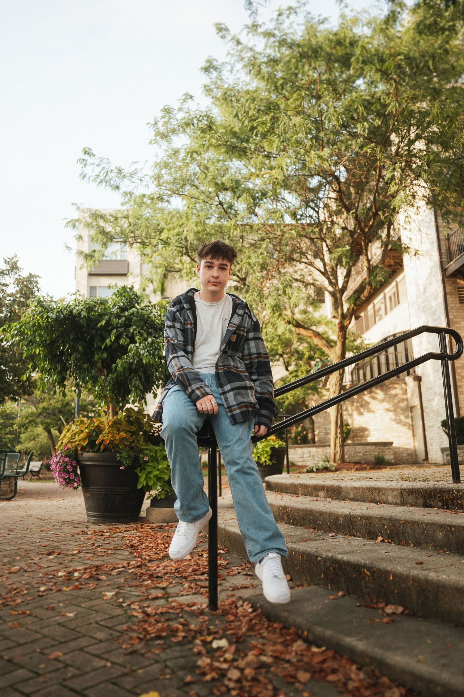 Person in casual attire sitting on outdoor steps with autumn leaves and trees in urban setting.