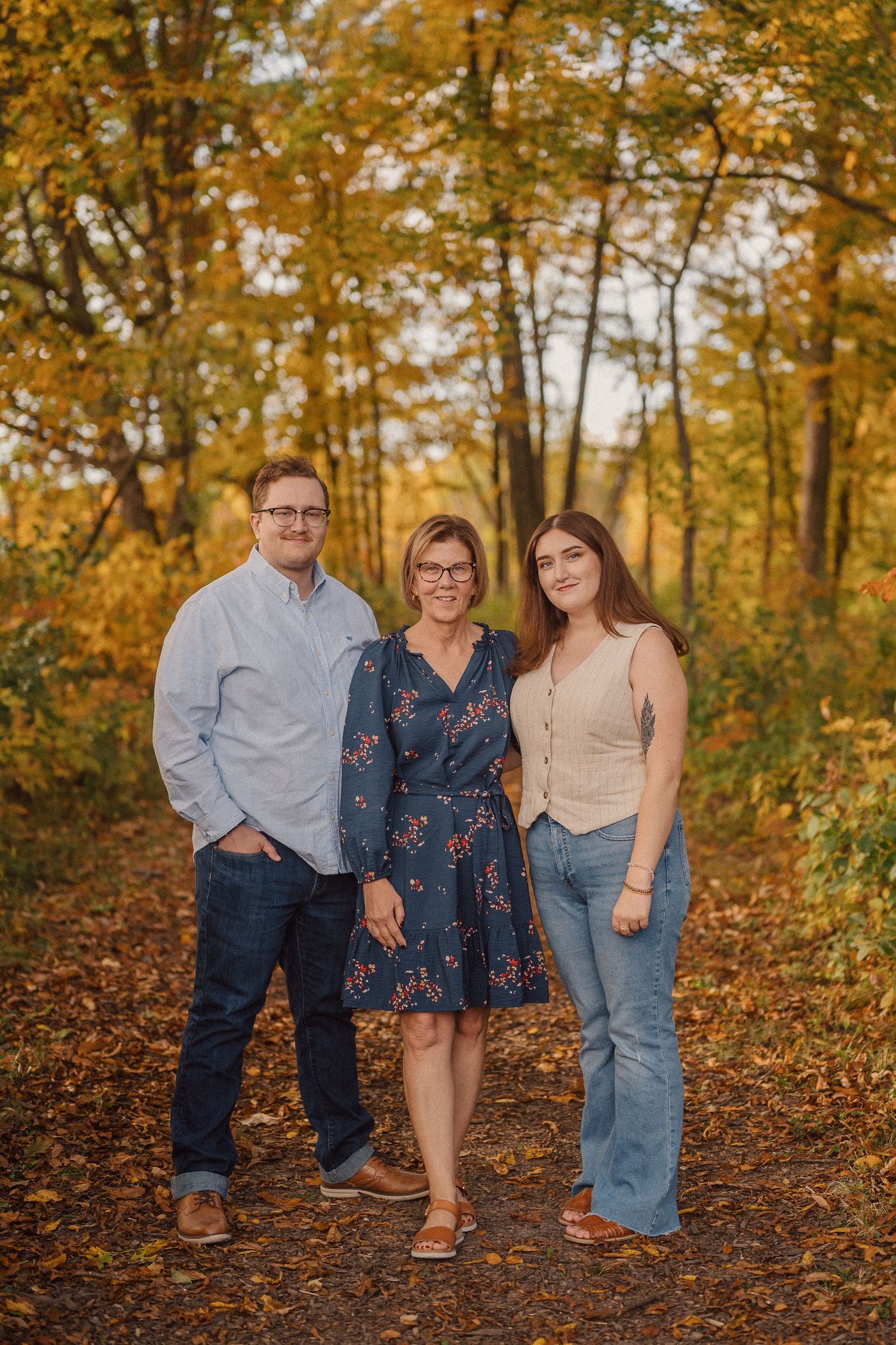 A group poses together in a wooded area with golden autumn foliage creating a warm backdrop.