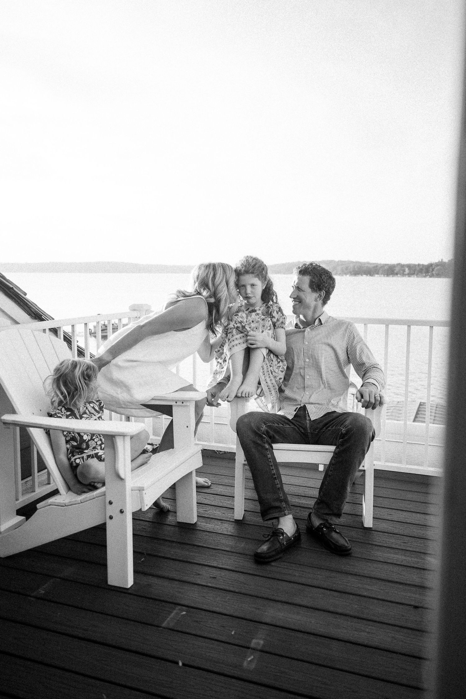 Playful couple interacts while sitting on a wooden deck overlooking the water.