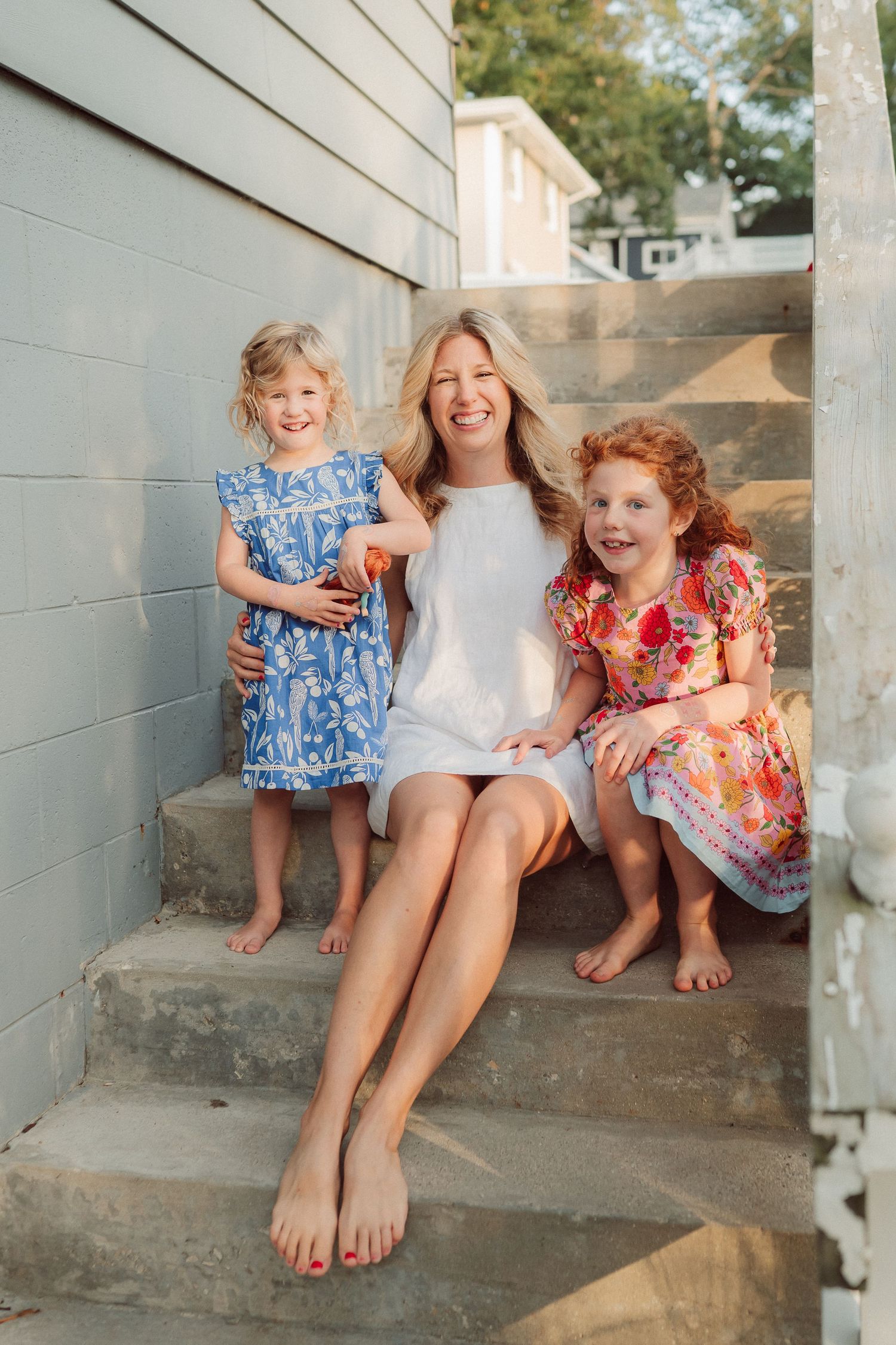 Three people share a candid laughing moment while sitting on concrete steps outdoors.