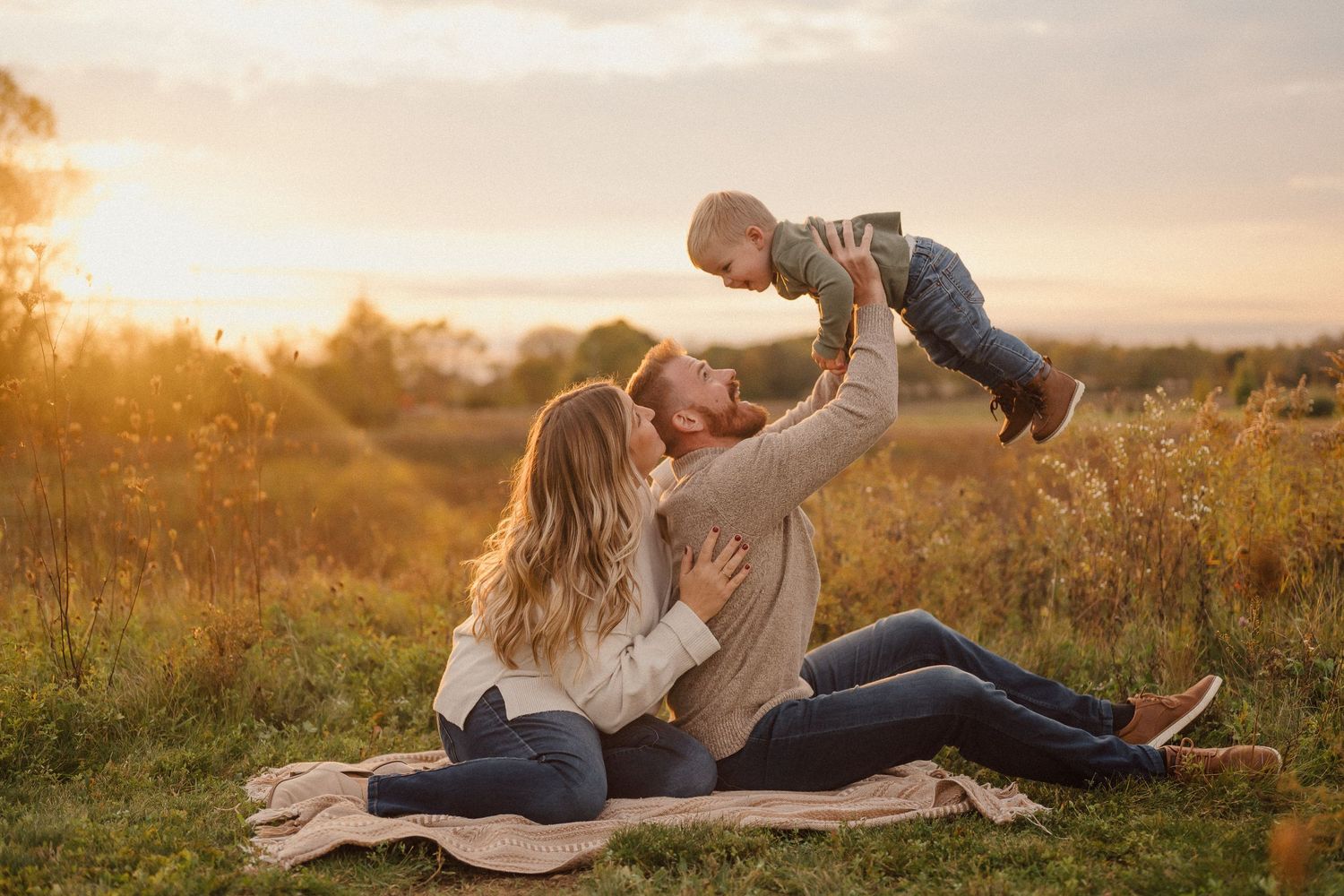 Family playing and embracing outdoors during a warm sunset photoshoot in nature.