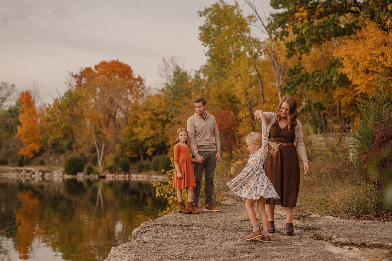 A couple walks along a scenic autumn path surrounded by golden foliage and trees near a tranquil lake.