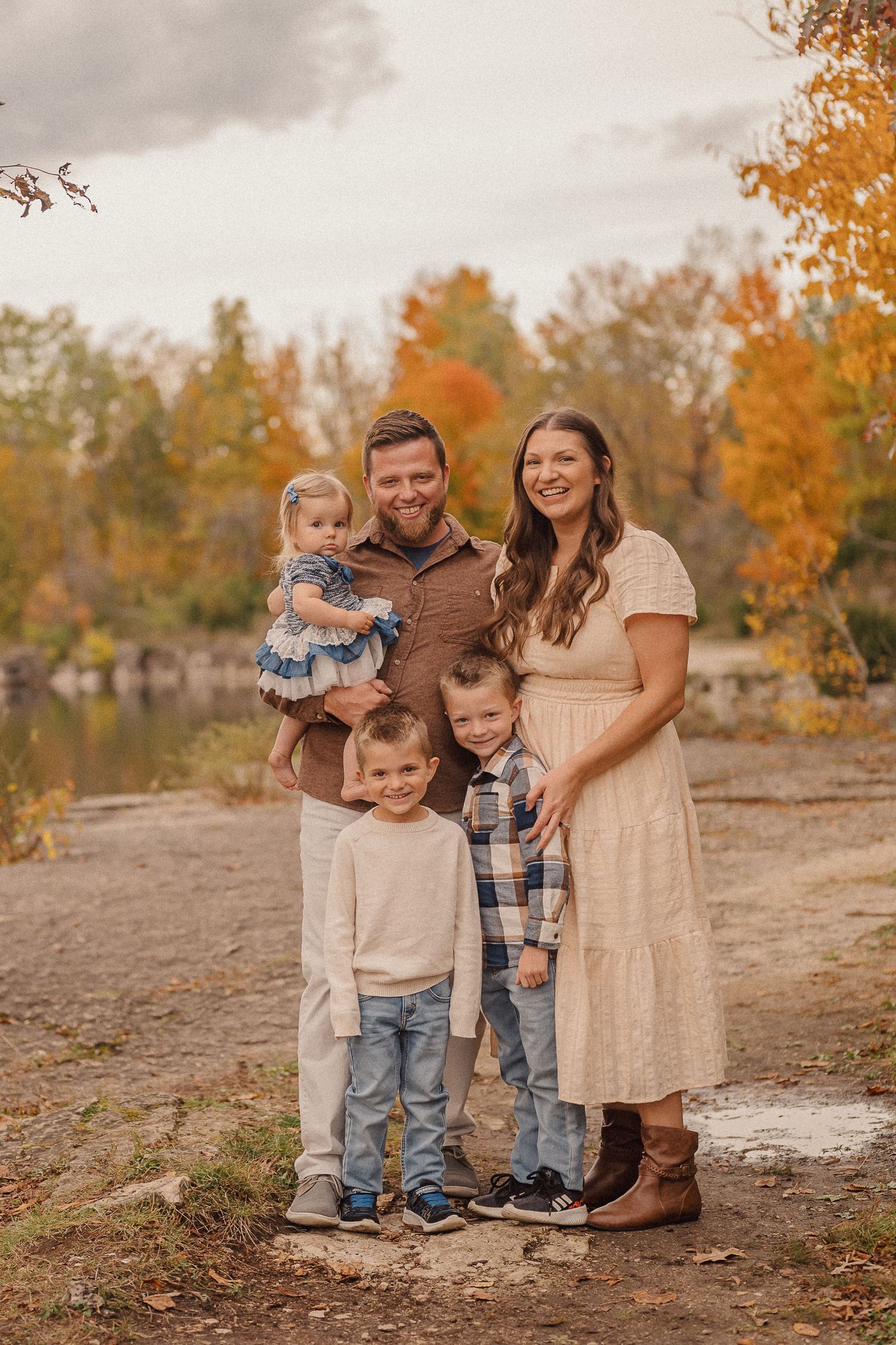 A family poses together outdoors on a fall day wearing coordinated neutral-toned outfits.