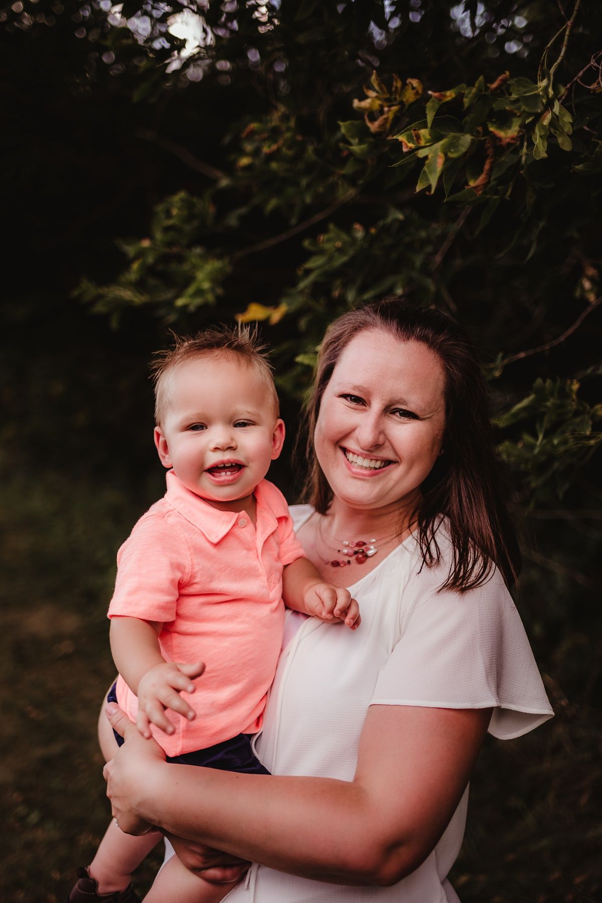 Outdoor family portrait with coral and white outfits against natural foliage background.