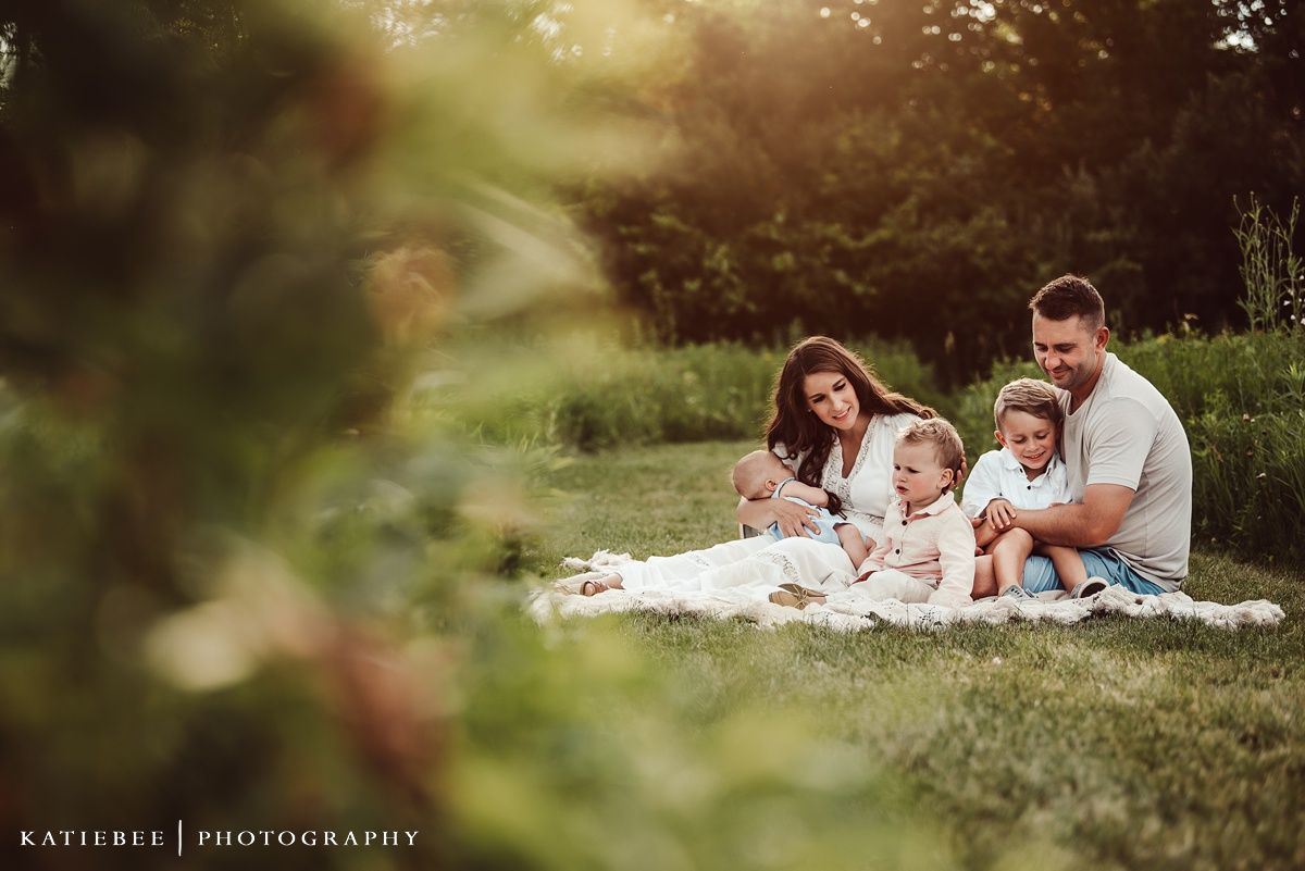 Family sitting together on blanket in grass during sunset photoshoot.