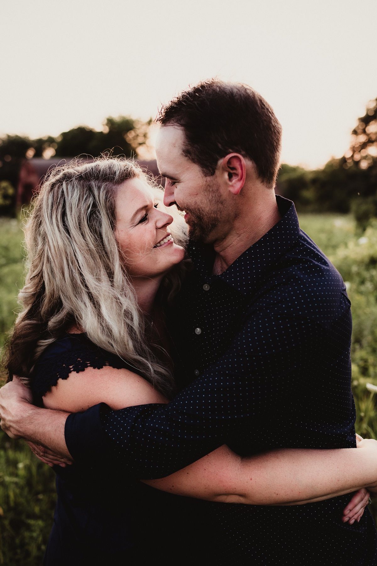 A romantic couple embraces and laughs together in a summer meadow during golden hour.