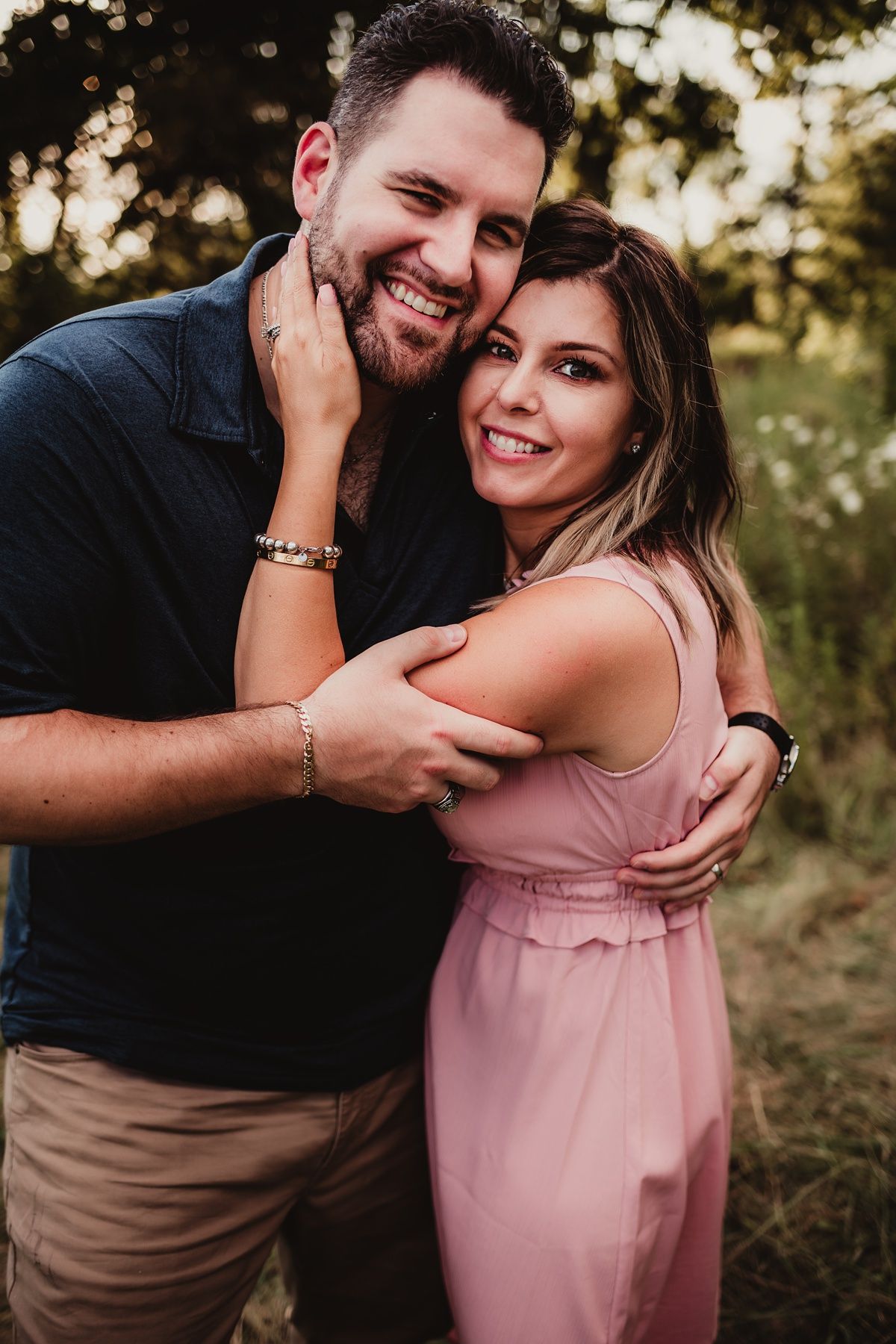 A romantic couple embraces and laughs together during a golden hour outdoor photoshoot in casual attire.