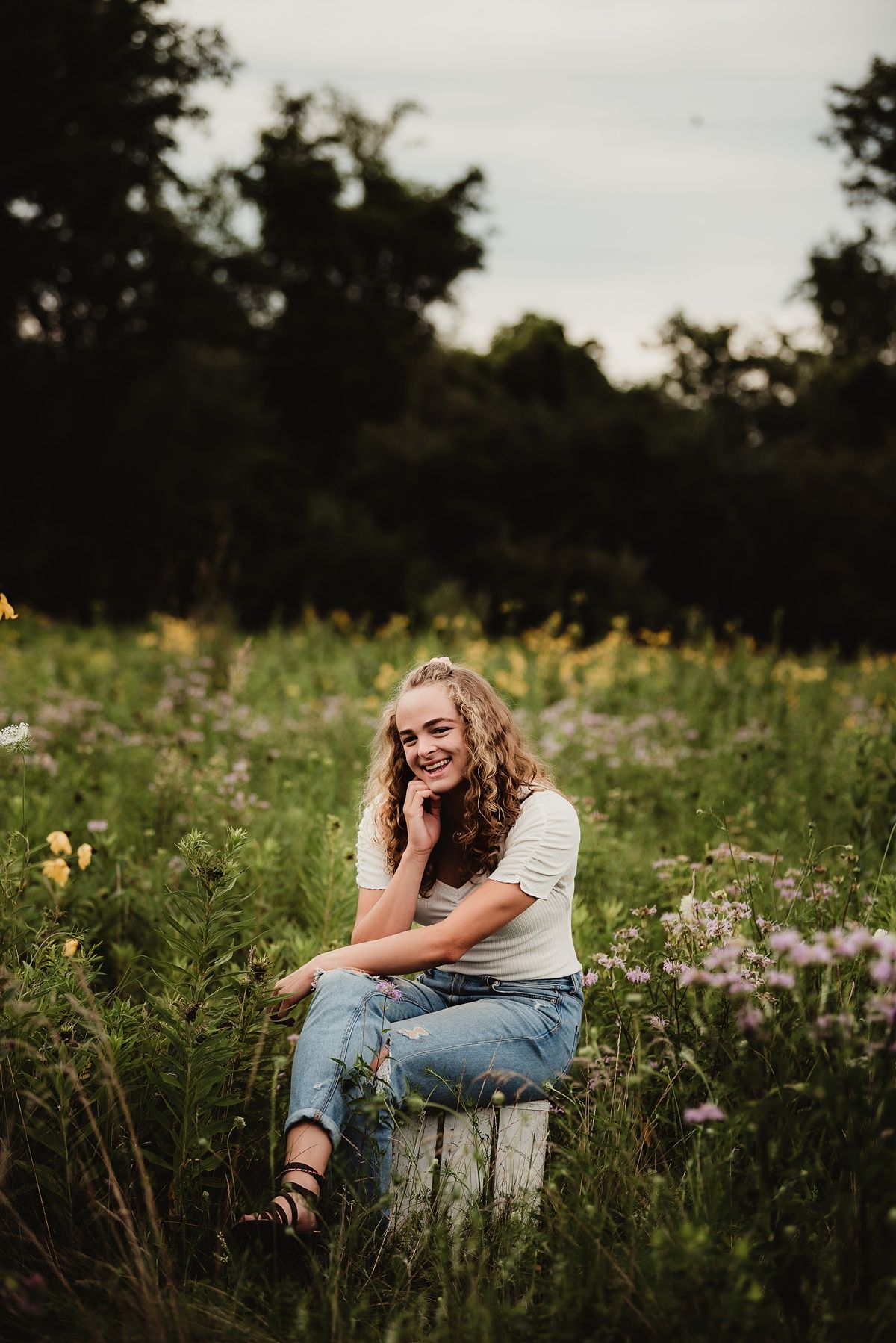 Person sitting on wooden crate in wildflower meadow at sunset.