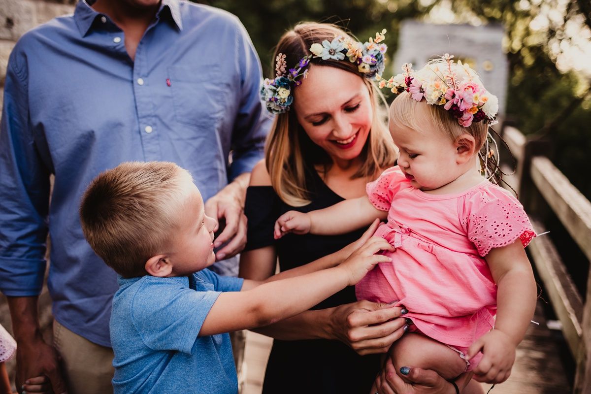 Family members share a tender moment outdoors with floral crowns and summer attire.