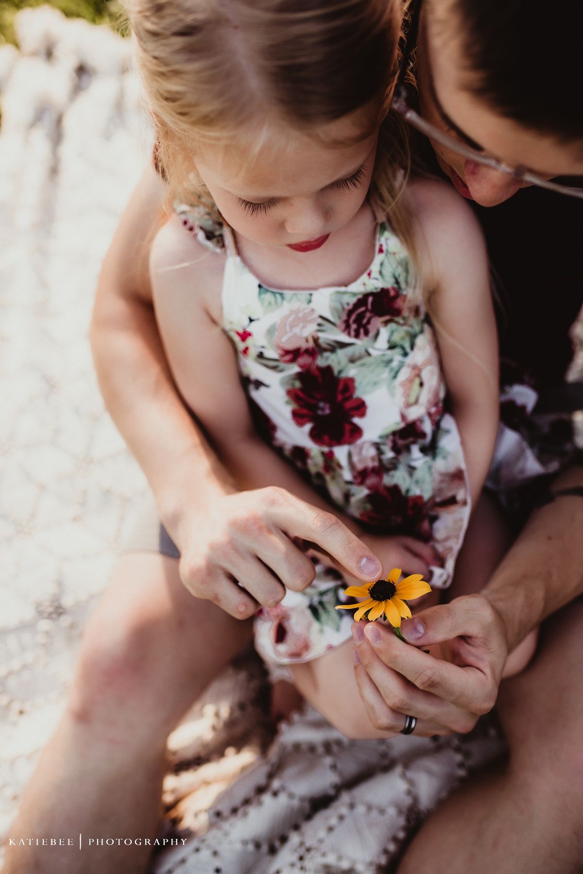 Family portrait on white blanket with sunset lighting and wildflowers in background.