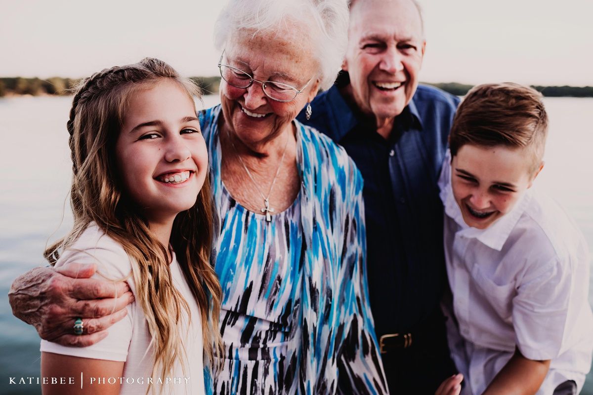 Joyful multi-generational group sharing laughs during lakeside family photoshoot.