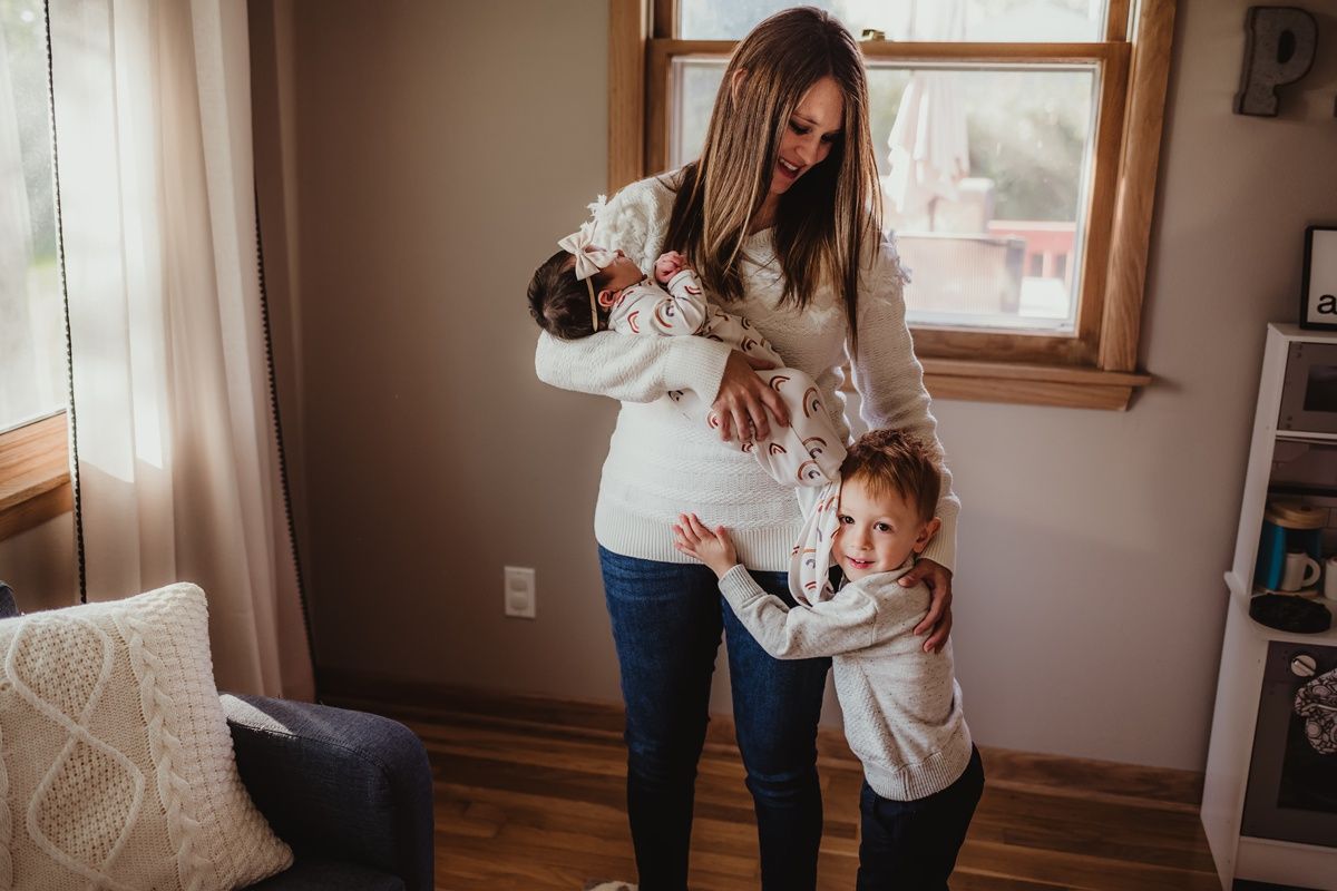 Mother and children in white sweaters sharing tender moment in sunlit room.