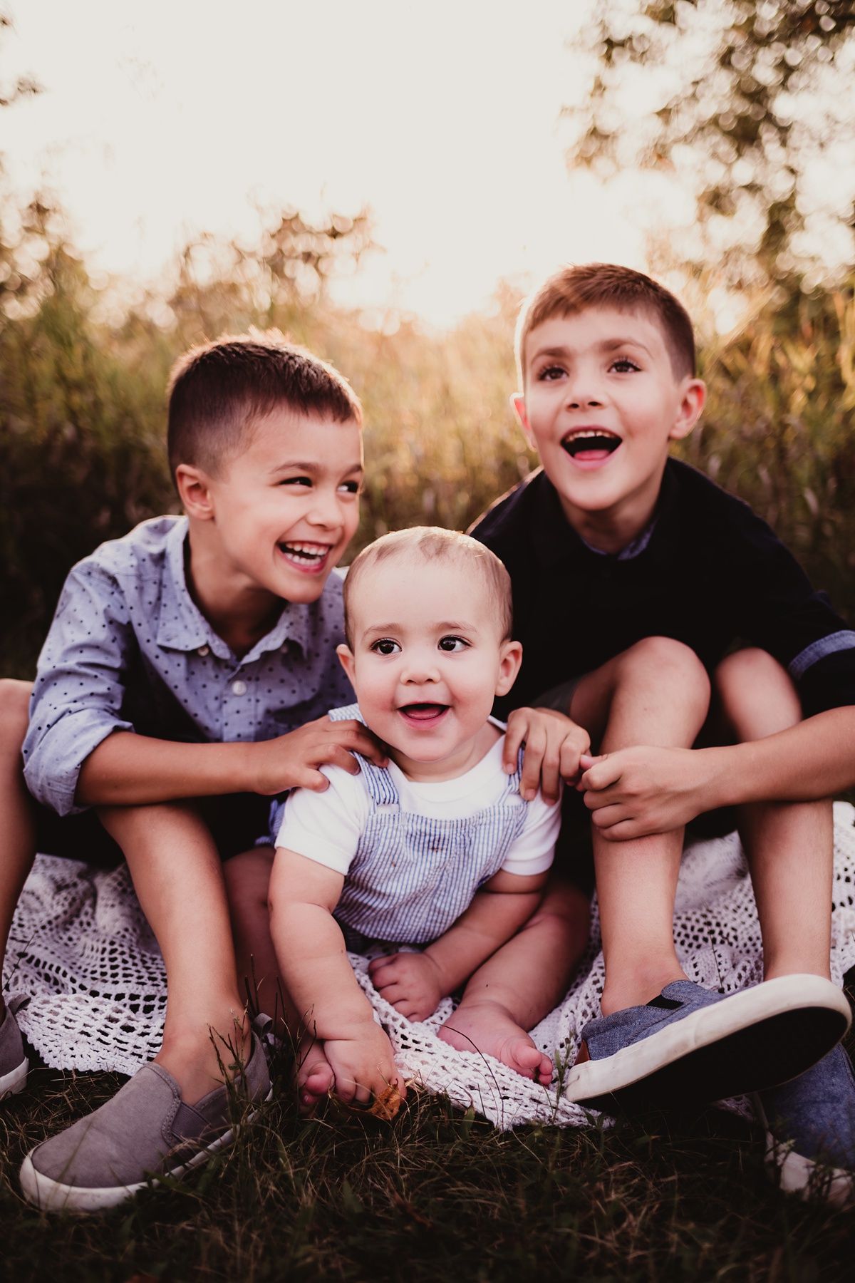 Three siblings sitting together outdoors with joyful expressions.