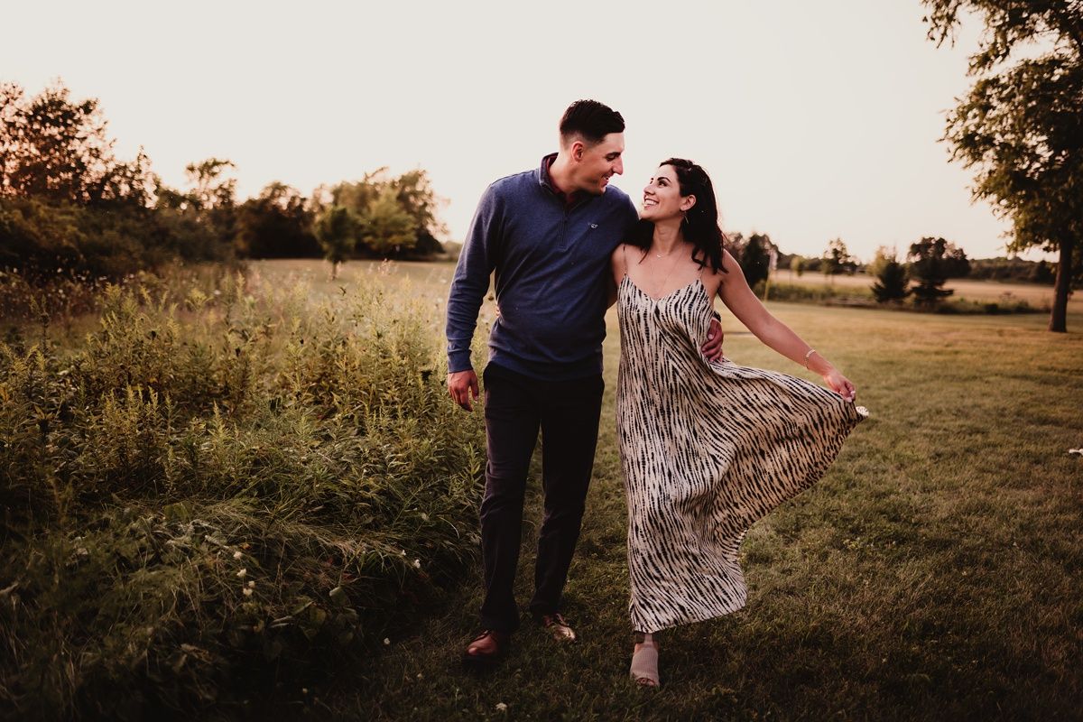 Couple walking through meadow at sunset in coordinated outfits.