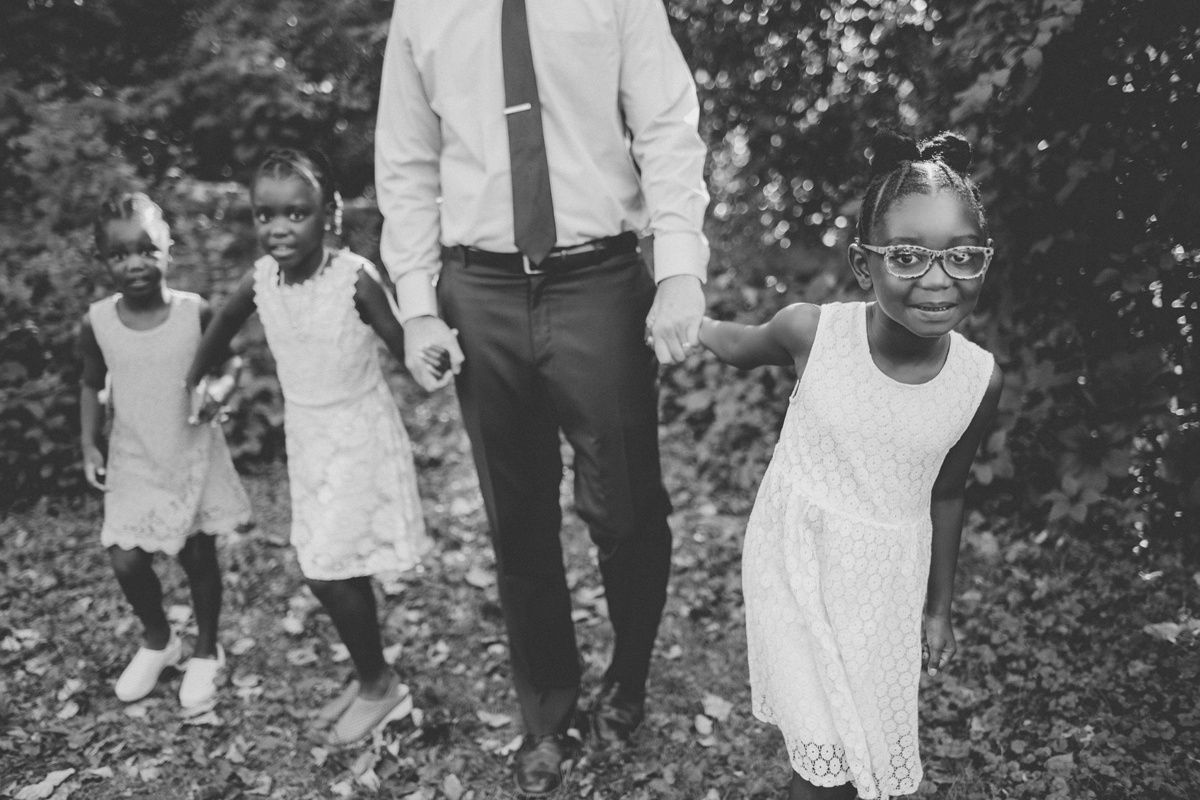 Black and white photo of children in white dresses walking with adult in outdoor setting.