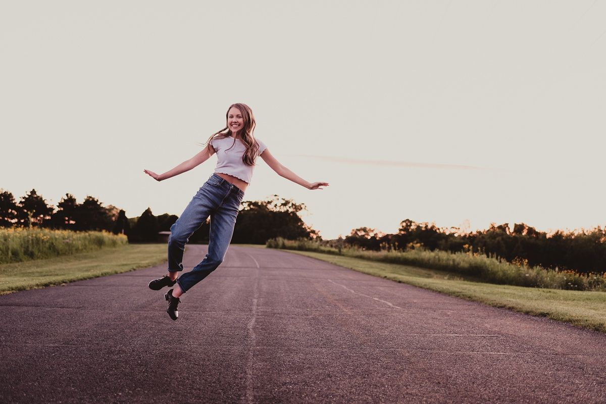 Someone jumping joyfully on an empty rural road at sunset.