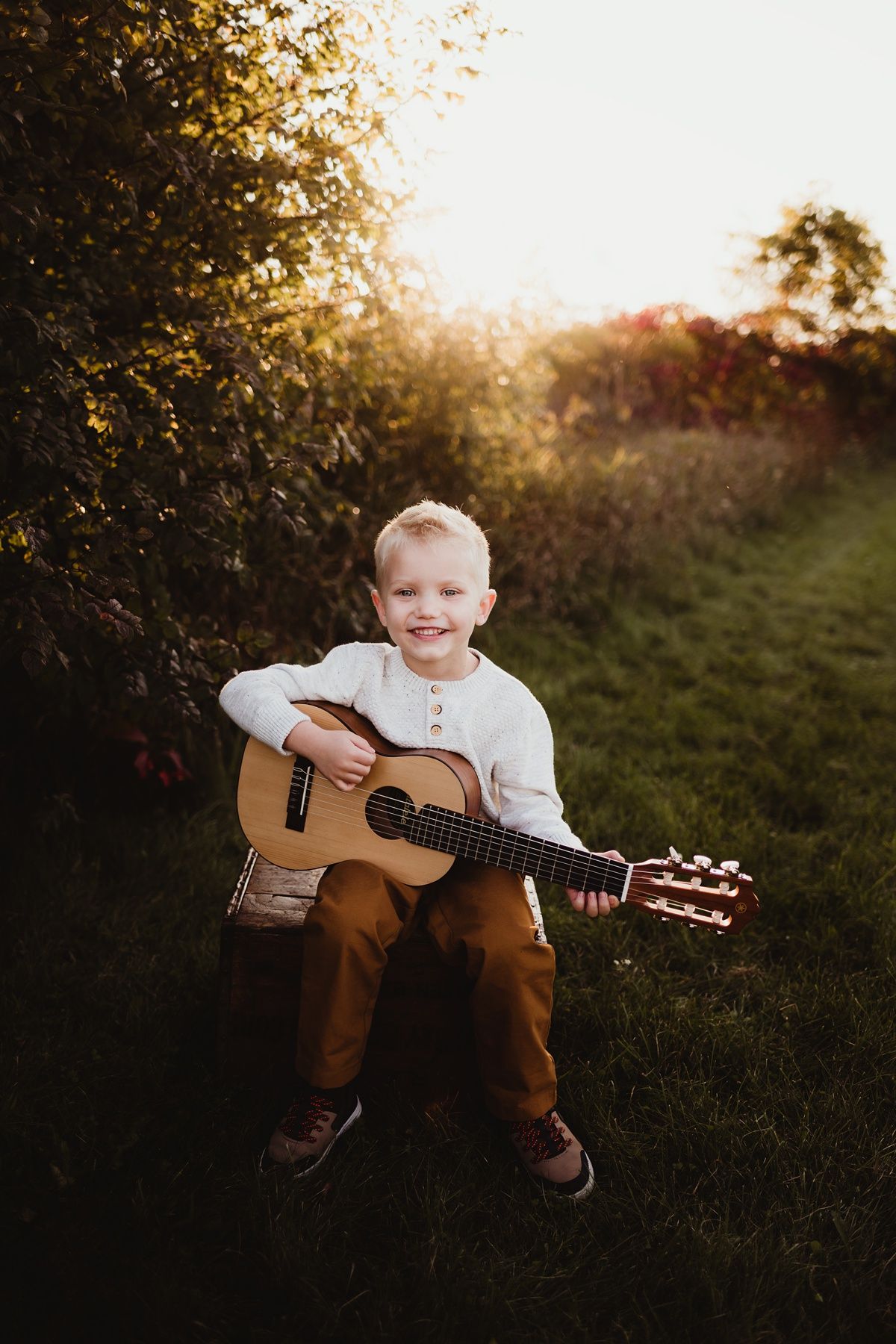 Child musician poses with acoustic guitar during golden hour outdoor portrait session.