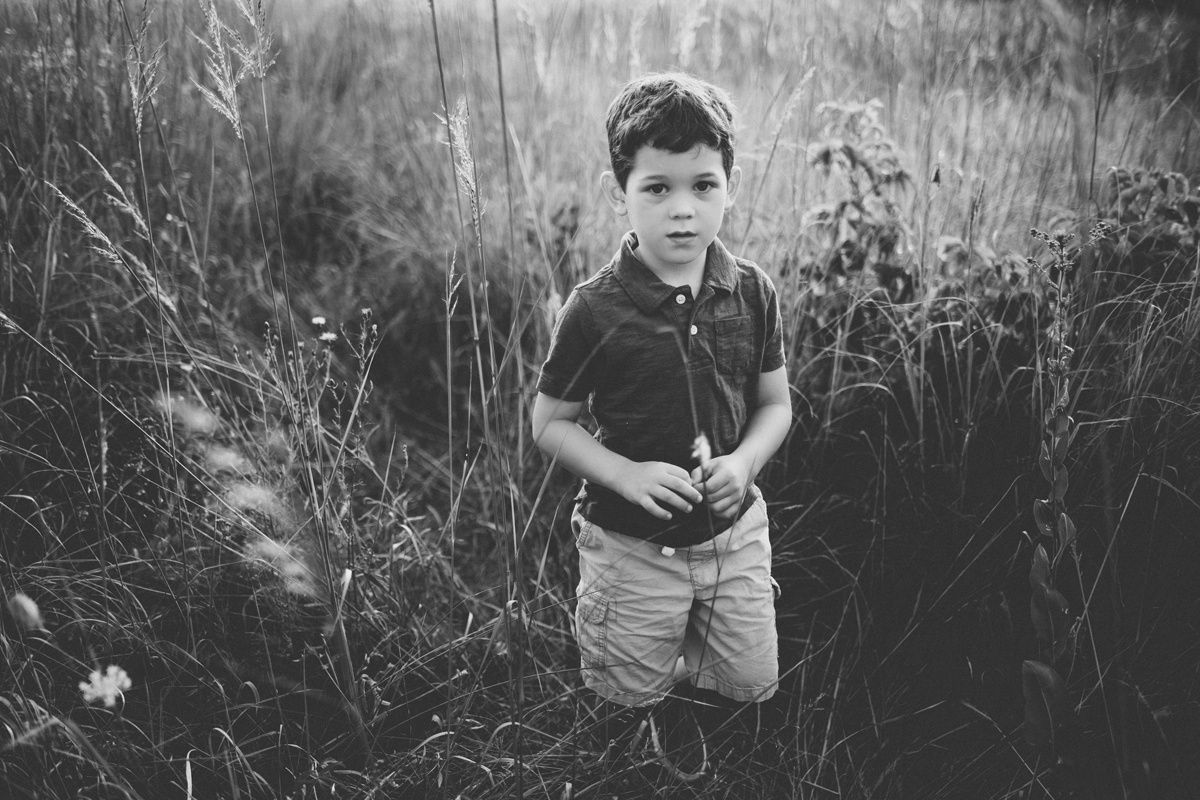 Black and white photo of a child standing among tall grass and wildflowers.