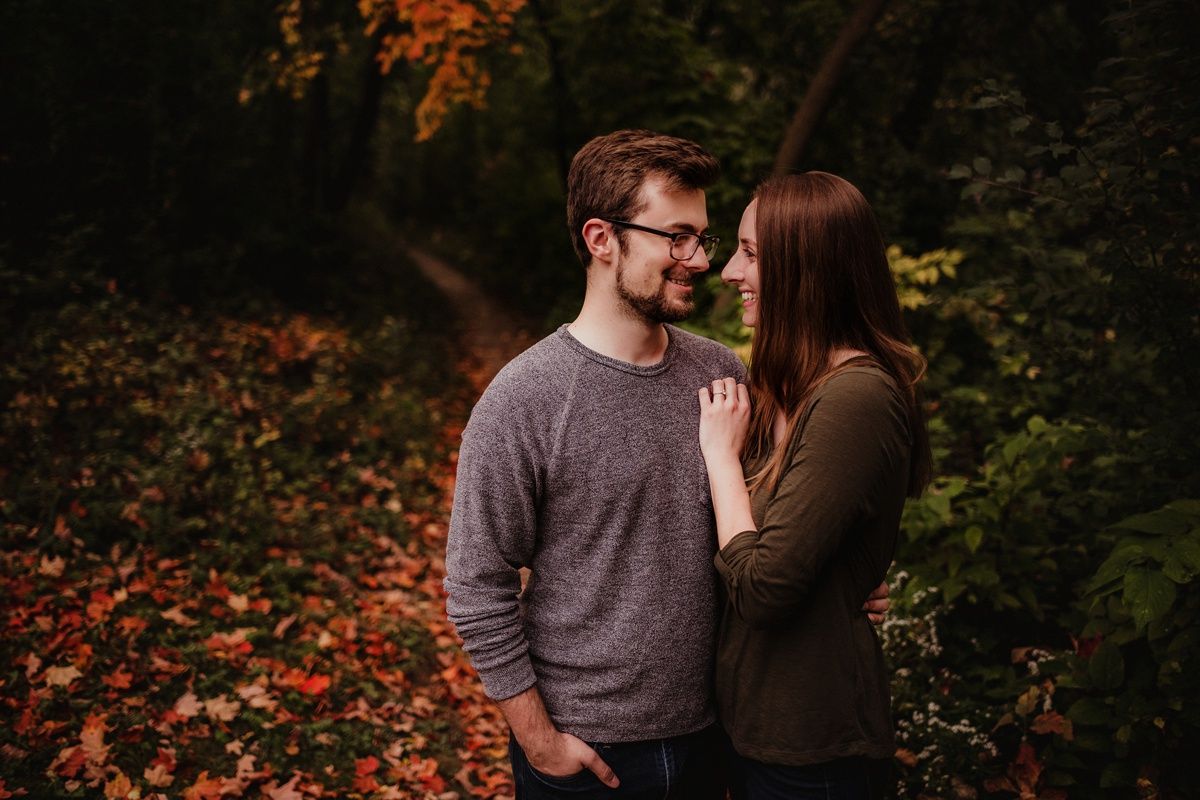 Couple in casual sweaters share intimate moment among autumn trees and fallen leaves.
