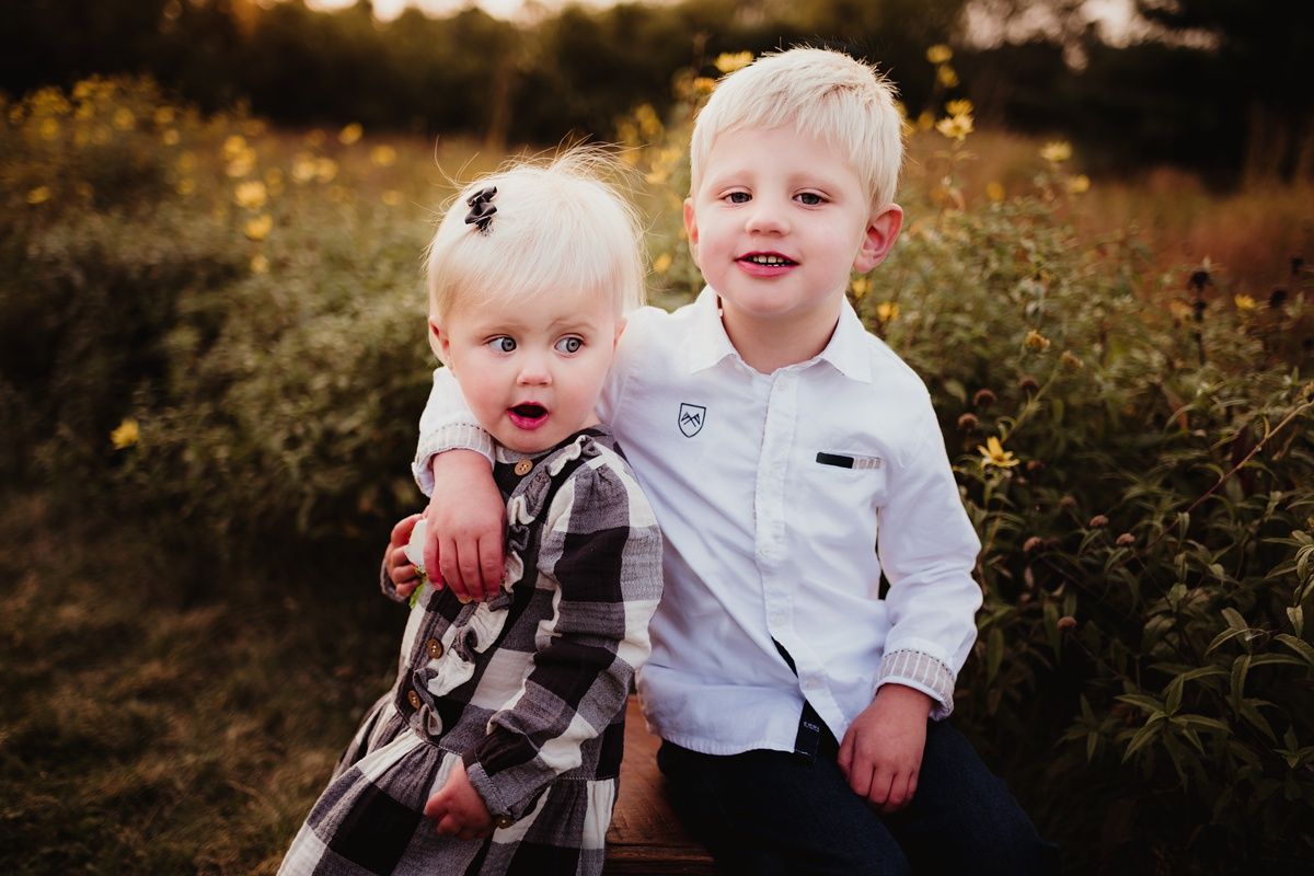 Two young children pose together in a wildflower field during sunset.