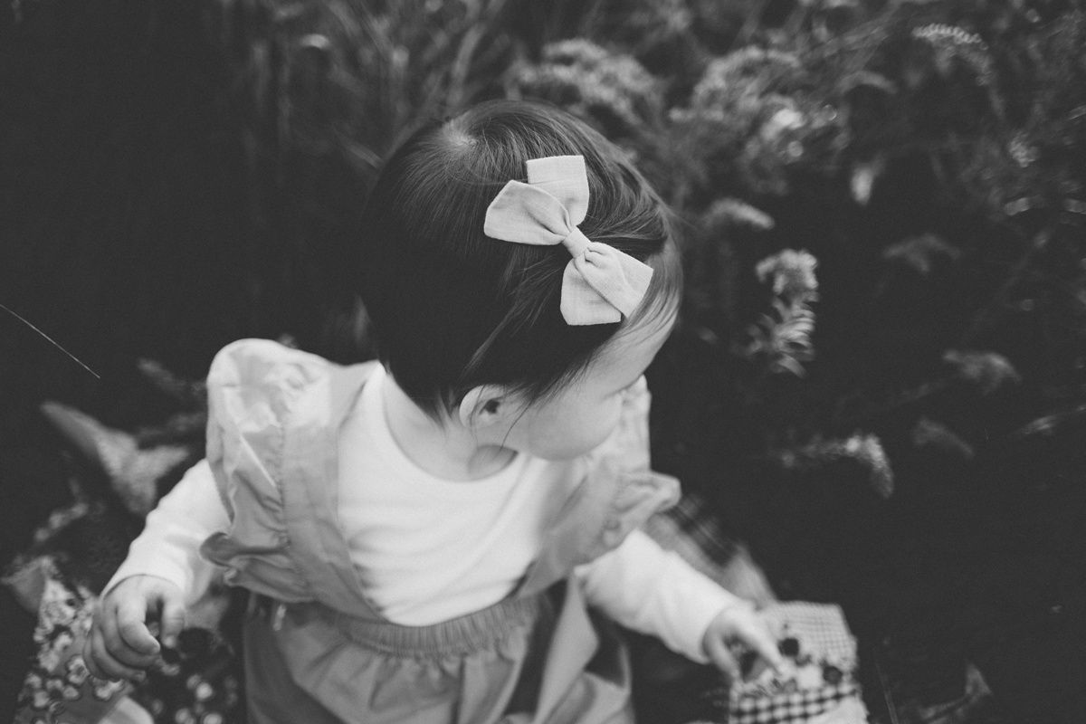 A child in a white dress and hair bows explores nature in black and white.