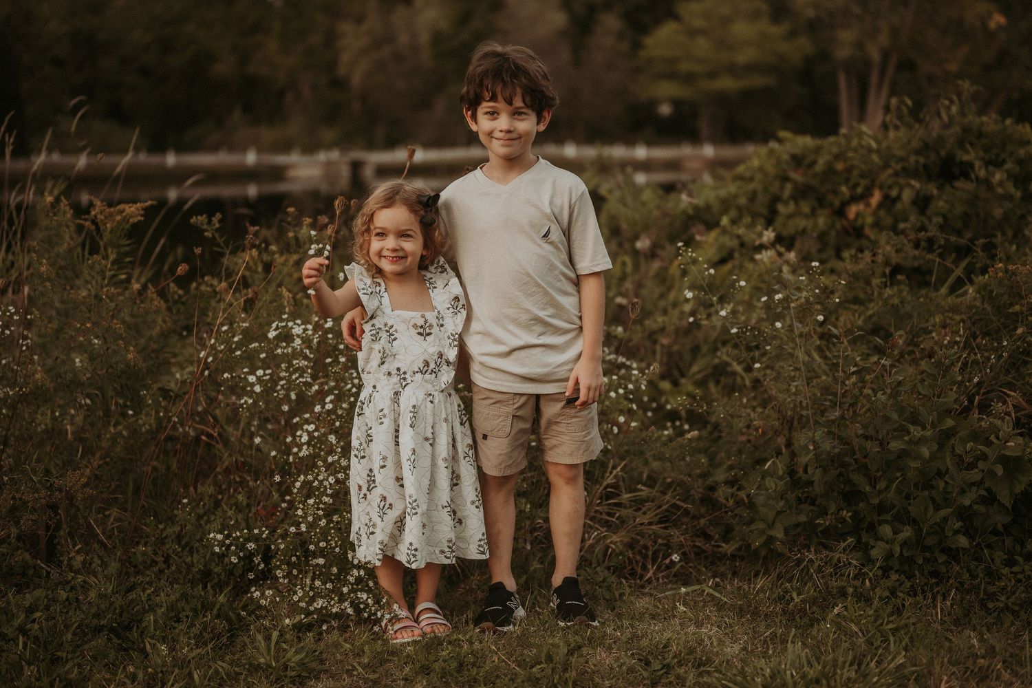 Two children standing together in a wildflower field during golden hour.