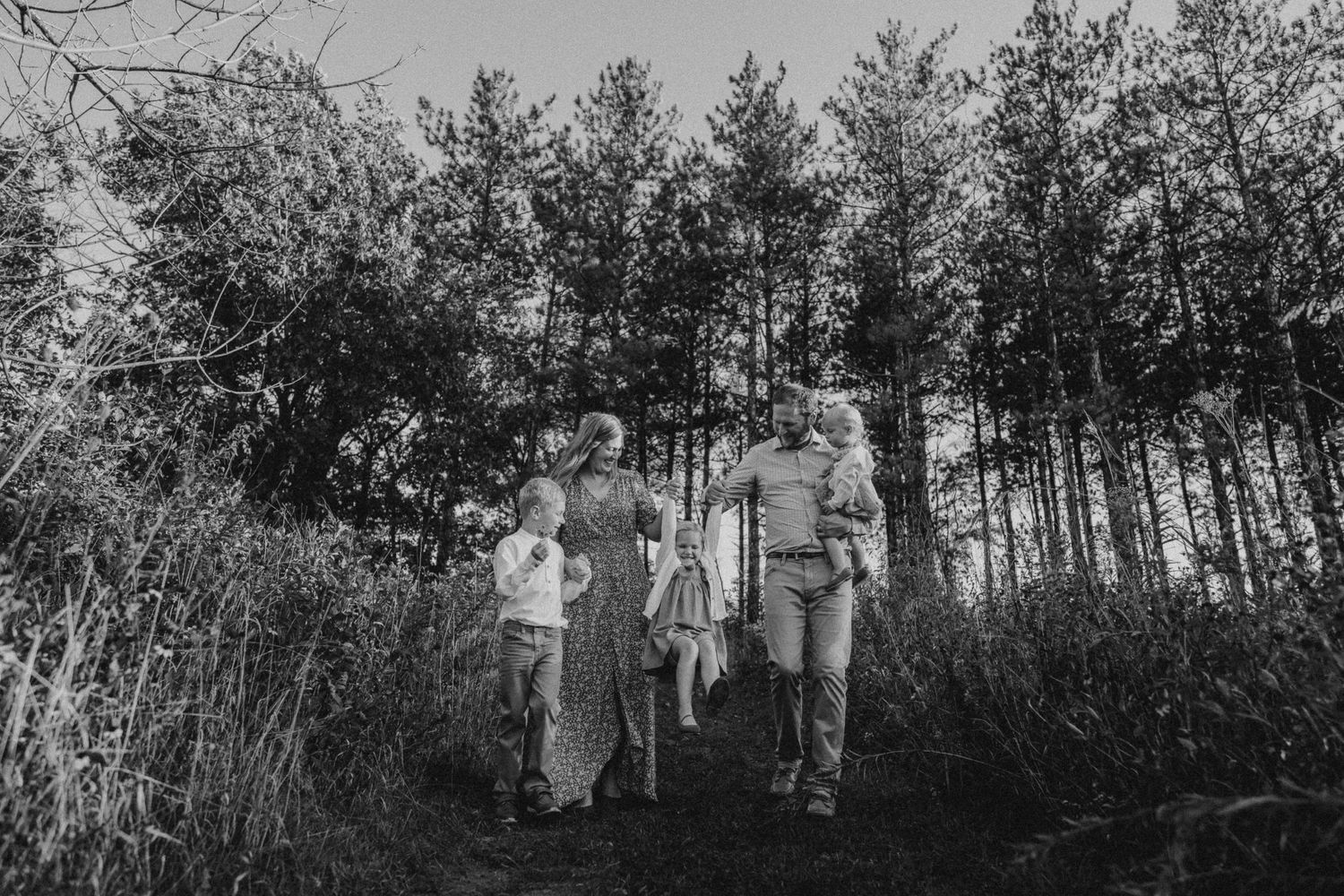 Black and white photo of a family walking together against a backdrop of tall pine trees.