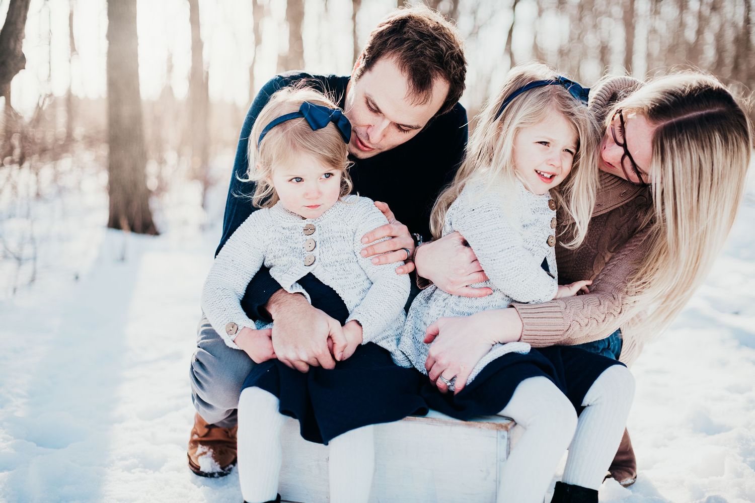 Winter family portrait in a snowy forest with parents cuddling their small children.