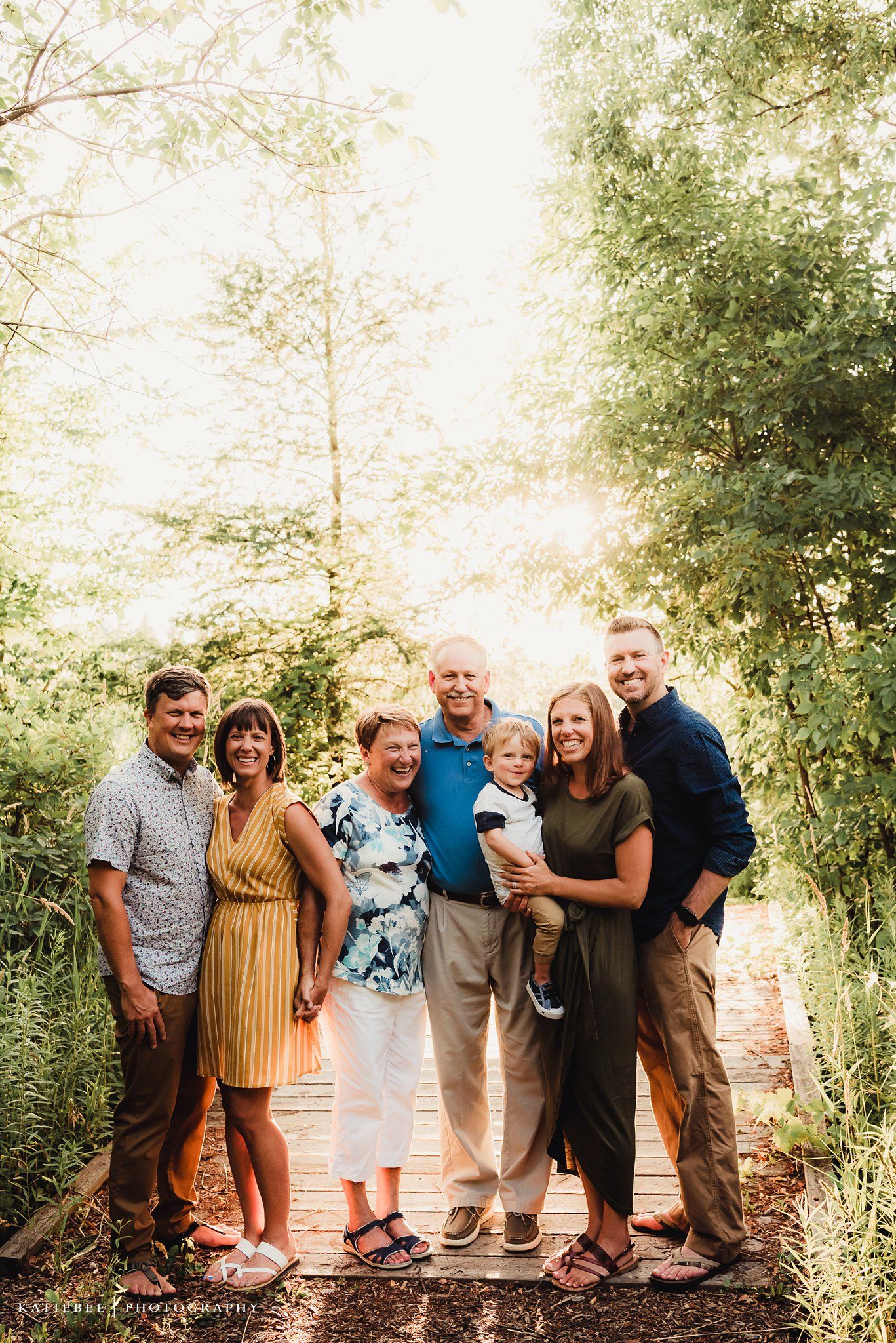 Extended family portrait on a wooden bridge surrounded by lush green trees.