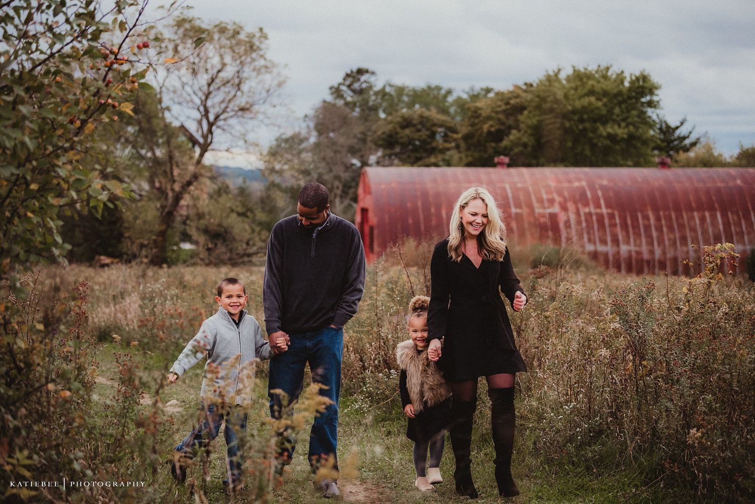 A family walking together through a field with a red barn structure visible behind them.