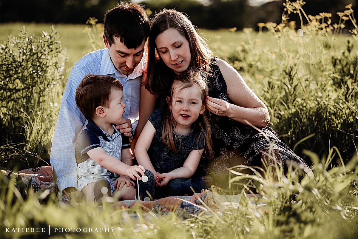 Family of four sharing laughs while cuddled together in a summer meadow.