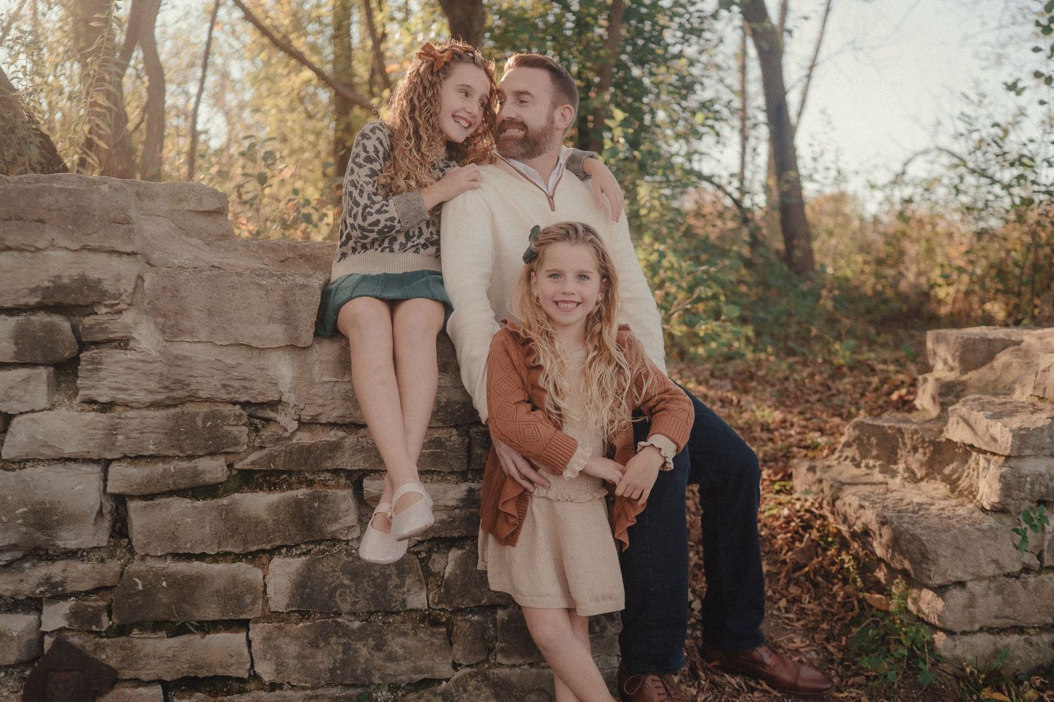Family members arranged casually on historic stone wall during fall outdoor photography session.