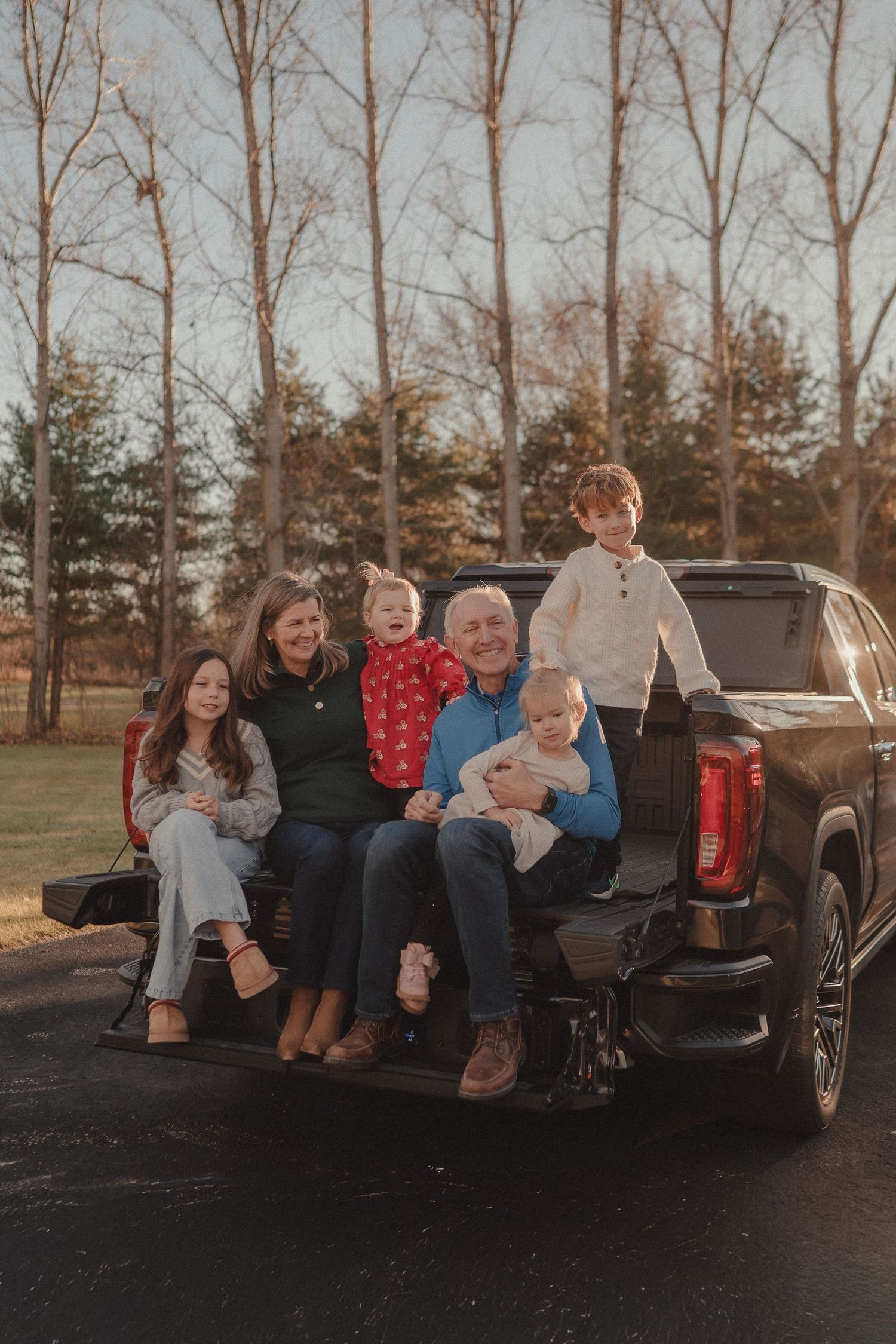 People sitting together in the back of a black pickup truck on an autumn afternoon.