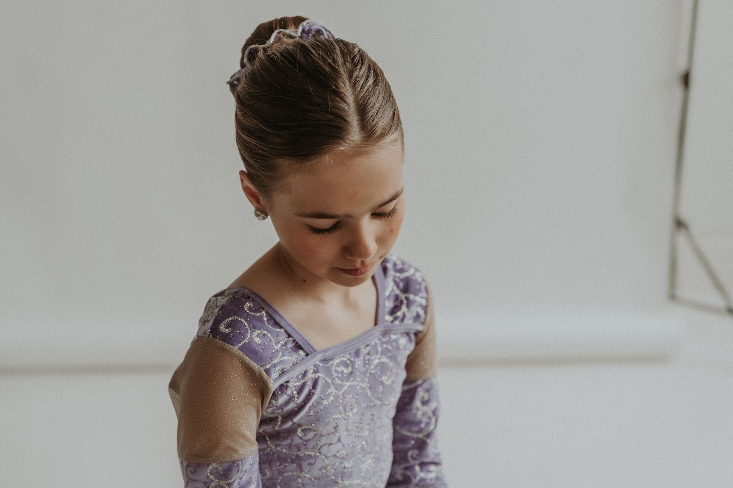 Dancer wearing a purple leotard looks down thoughtfully during a portrait session.
