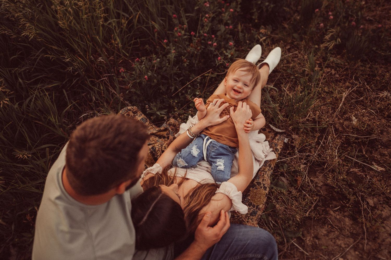 Playful family moment captured from above as they lie on a blanket in nature.