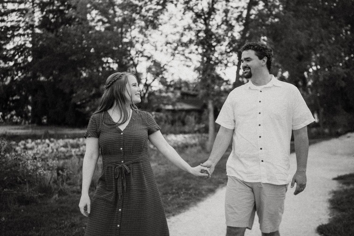 Black and white photo of a couple walking hand in hand on a garden path.