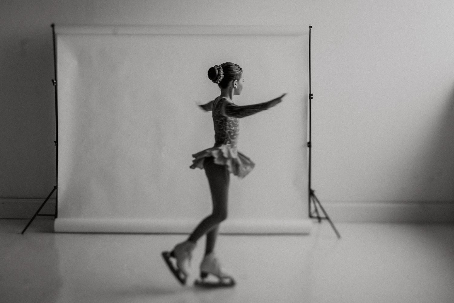 Silhouetted figure in a tutu and ice skates performs a graceful skating pose against a white studio backdrop.