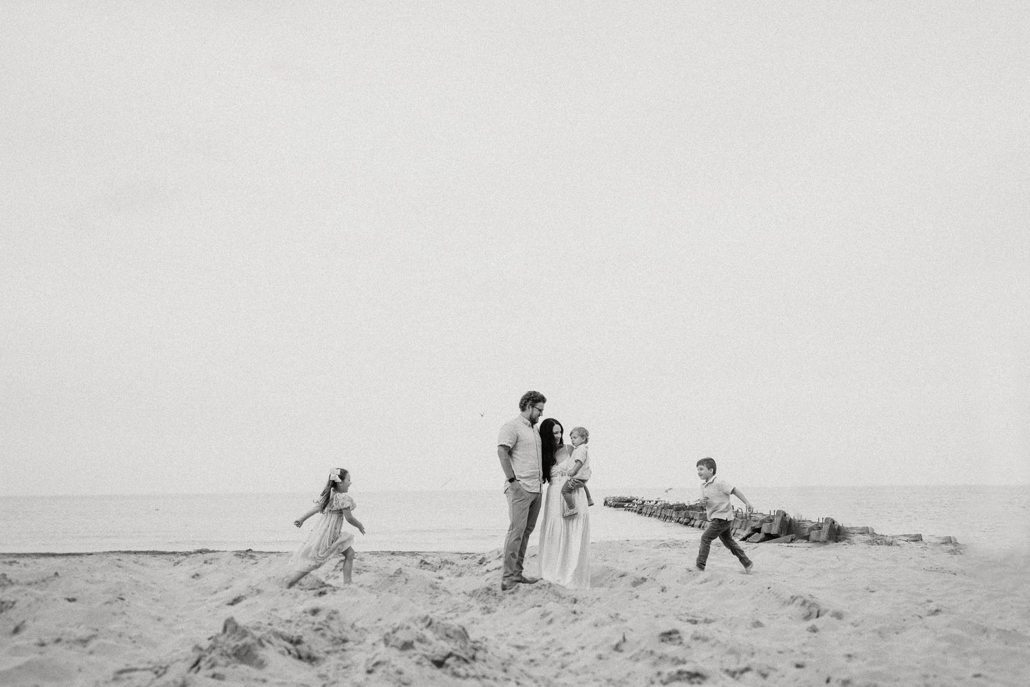 Family group poses on sandy beach with horizon in background.