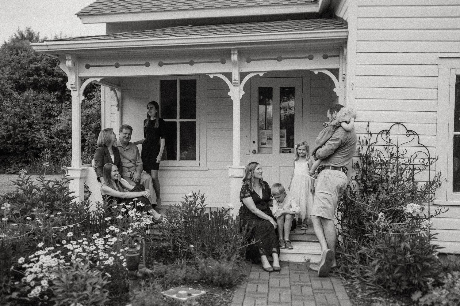 A vintage-style black and white photo of a group gathered on a charming farmhouse porch.