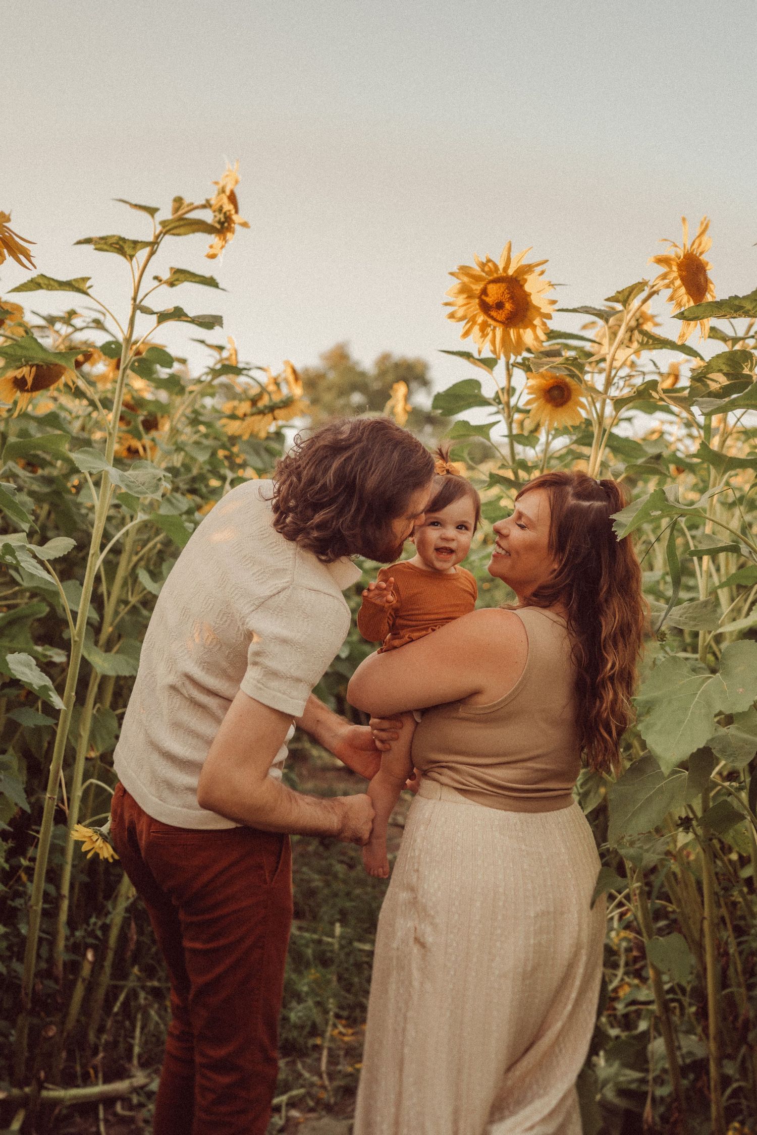 A loving family shares a tender moment in a sunlit field of towering sunflowers.